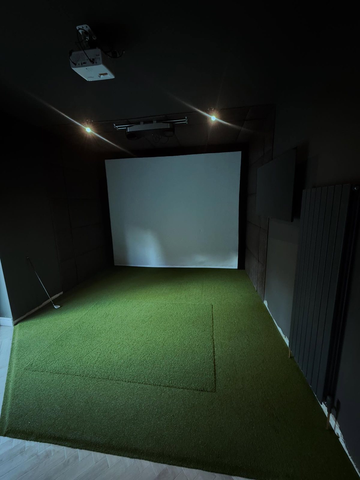 Finished home golf simulator room with turf and projector screen